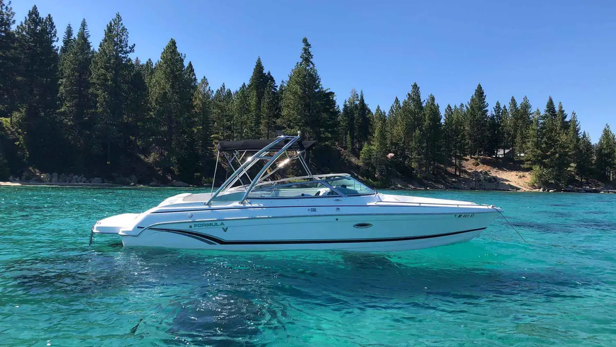 A white bowrider anchored in clear turquoise water off a pine-lined beach on Lake Tahoe