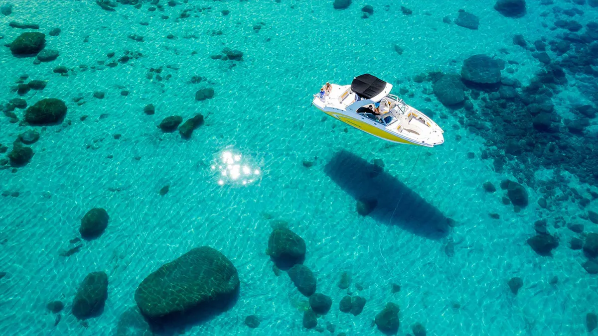 A small motor boat seen from above over clear water and boulders on Lake Tahoe