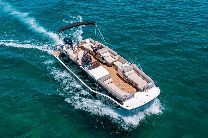 A pontoon boat with guests speeding across turquoise water on Lake Tahoe, seen from above