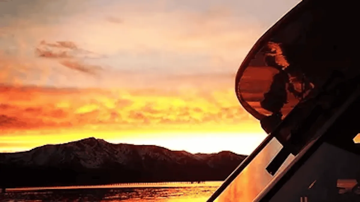 An orange sunset over the mountains seen past the rail of a yacht on Lake Tahoe
