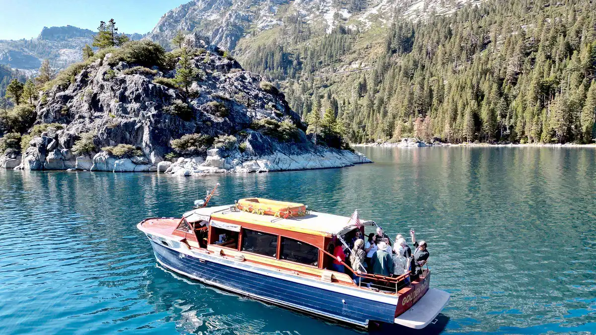 The varnished Golden Rose wooden water taxi with guests aboard beside the granite shore of Fannette Island