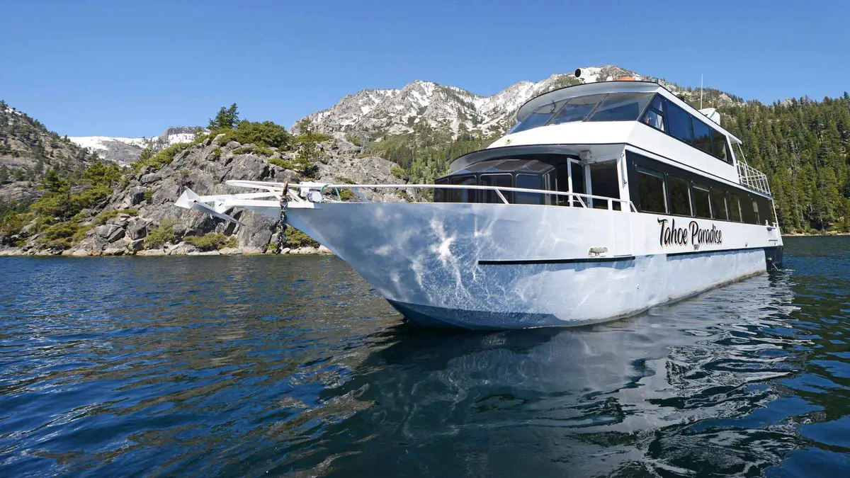 The white two-level Tahoe Paradise yacht on Lake Tahoe near a granite shoreline