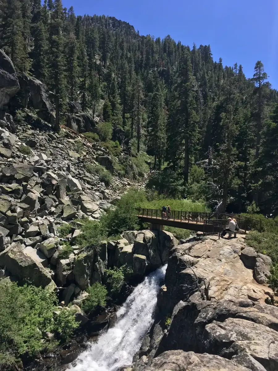 Upper Eagle Falls pouring over granite ledges under pines, with a footbridge above the cascade