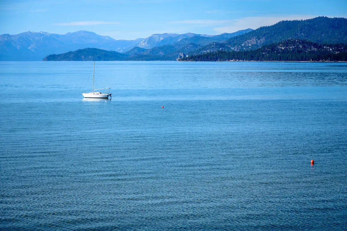 A single sailboat on open blue Lake Tahoe with forested mountains behind